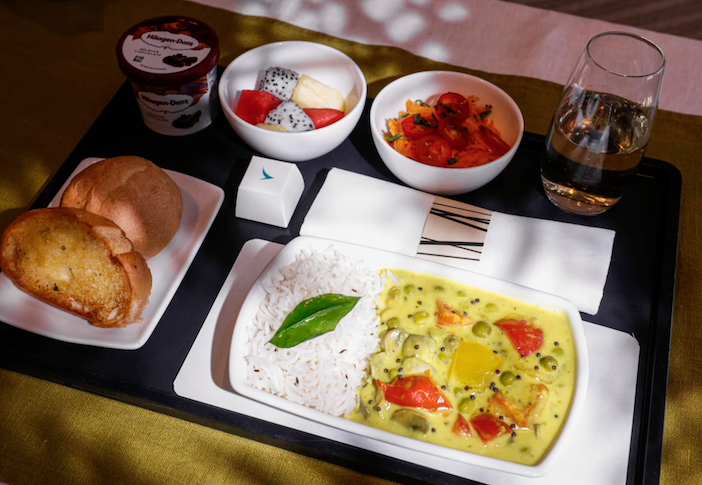 An inflight meal tray with Premium Economy Meal - Bombay carrot salad with cashews, raisins and cherry tomatoes & Keralan-style coconut curry with mushrooms, red bell peppers and cumin rice